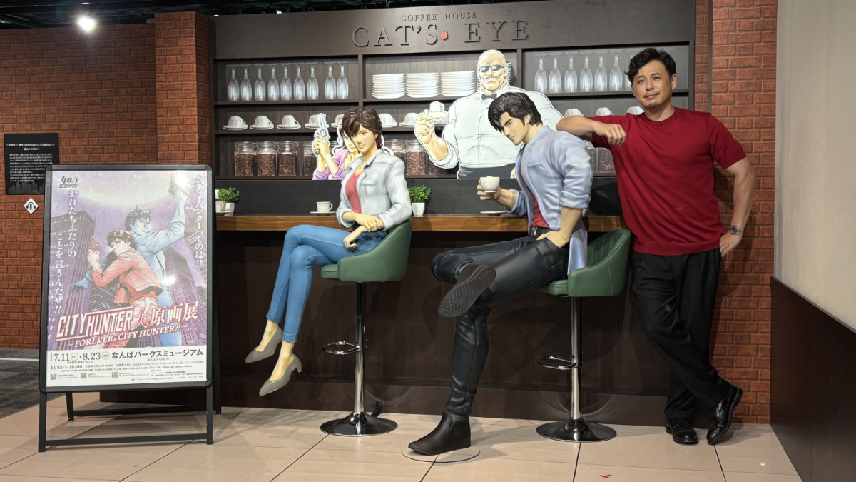 シティーハンター大原画展のポスターと喫茶キャッツアイ展示の前に立つ平子祐希さん