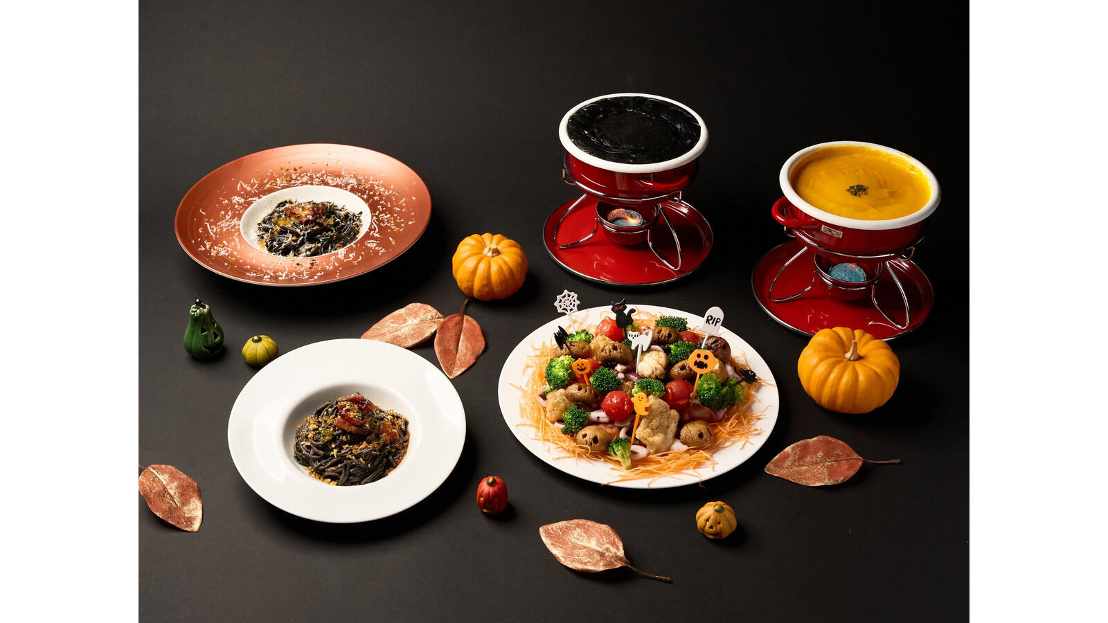 ハロウィンの飾り付けを背景に並ぶパスタやチーズフォンデュなどの料理