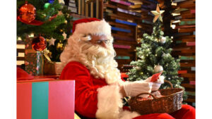 クリスマスツリーの横に座り、小物を手に持つ赤い衣装のサンタクロース